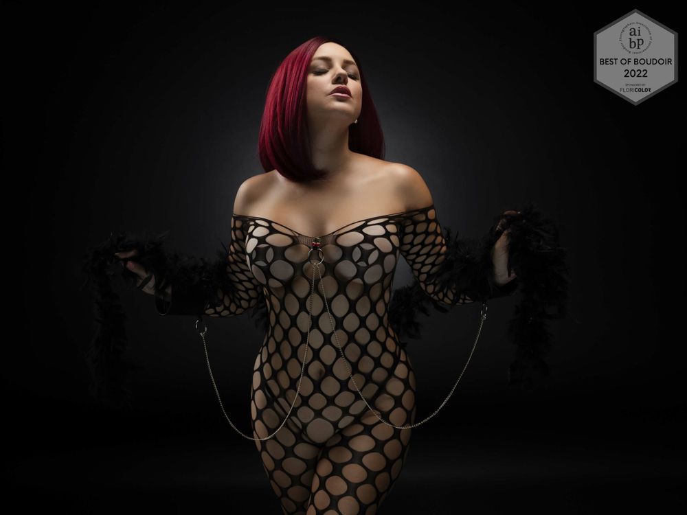 A person in a black fishnet bodysuit poses dramatically against a dark background in a fashion photoshoot series.