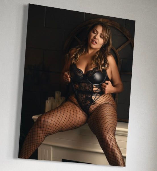Woman in black lace lingerie and fishnet stockings posing elegantly in a dimly lit room.