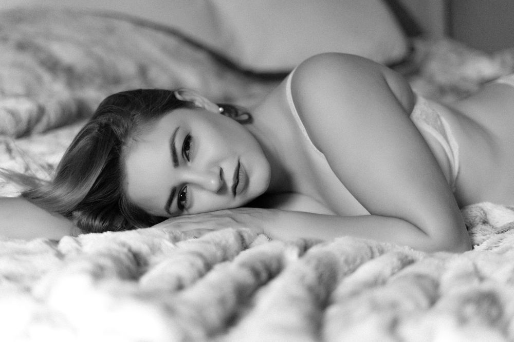 Sensual black and white boudoir photography on white bedding with soft lighting.