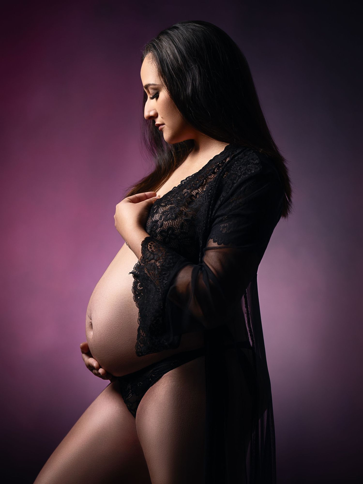Maternity portraits in black lace against purple backdrop showing pregnancy silhouette.