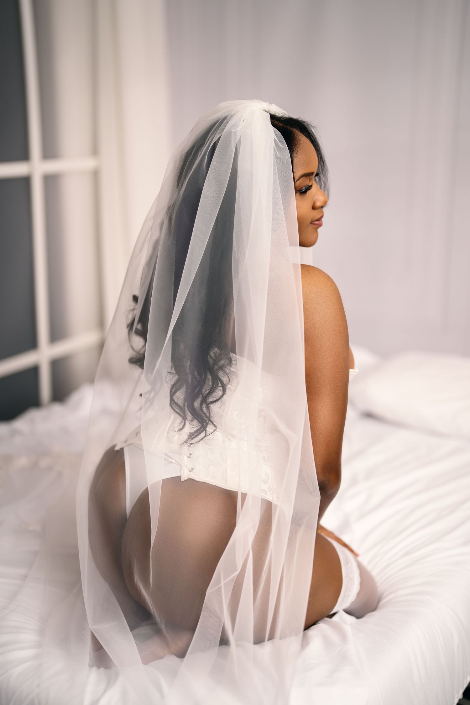 Artistic boudoir photography series featuring a bride in white veil against soft ethereal lighting and white bedding.