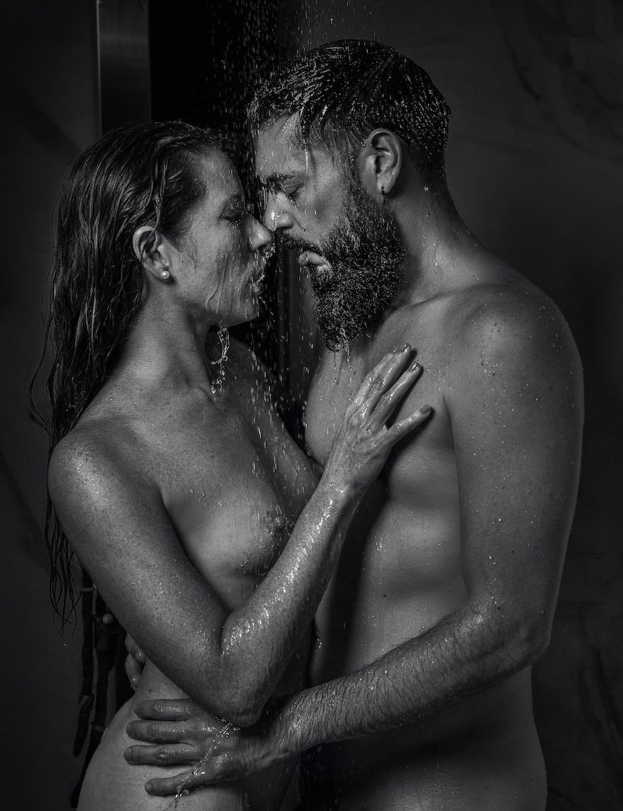 Black and white photo of a romantic couple embracing intimately under shower water droplets.
