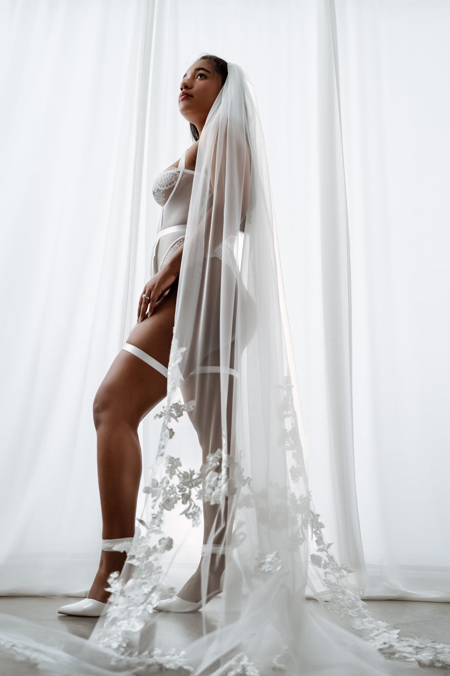 Artistic bridal boudoir  photo series showing silhouette against white curtains with flowing bridal veil and floral details. Best Bridal