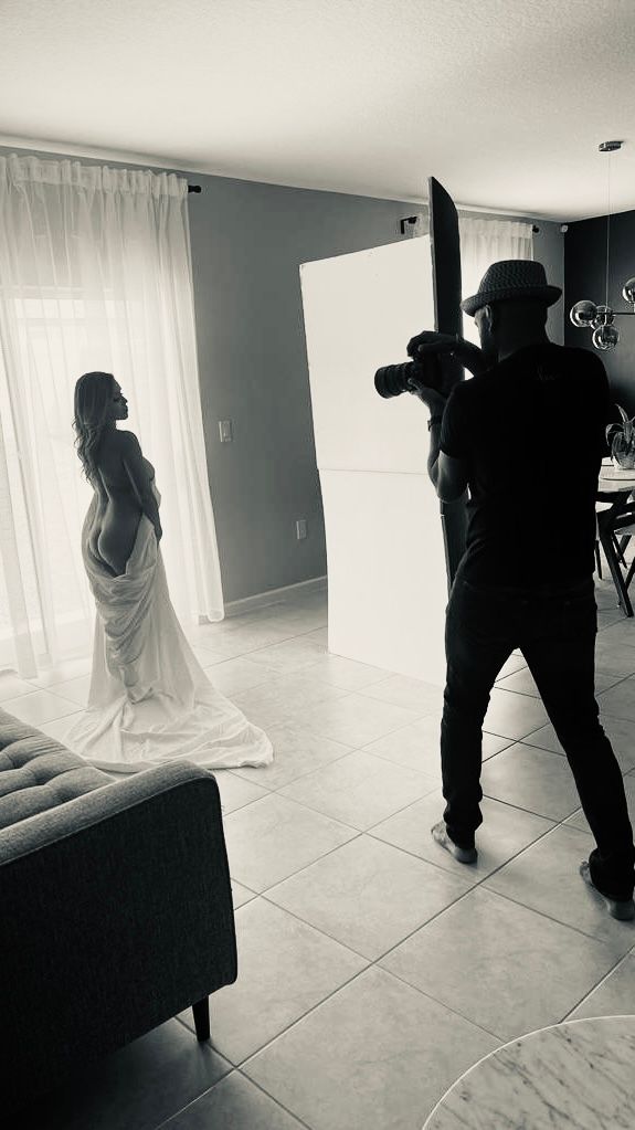 A photographer captures a dramatic bridal session in a bright white room with flowing fabric and natural window light.