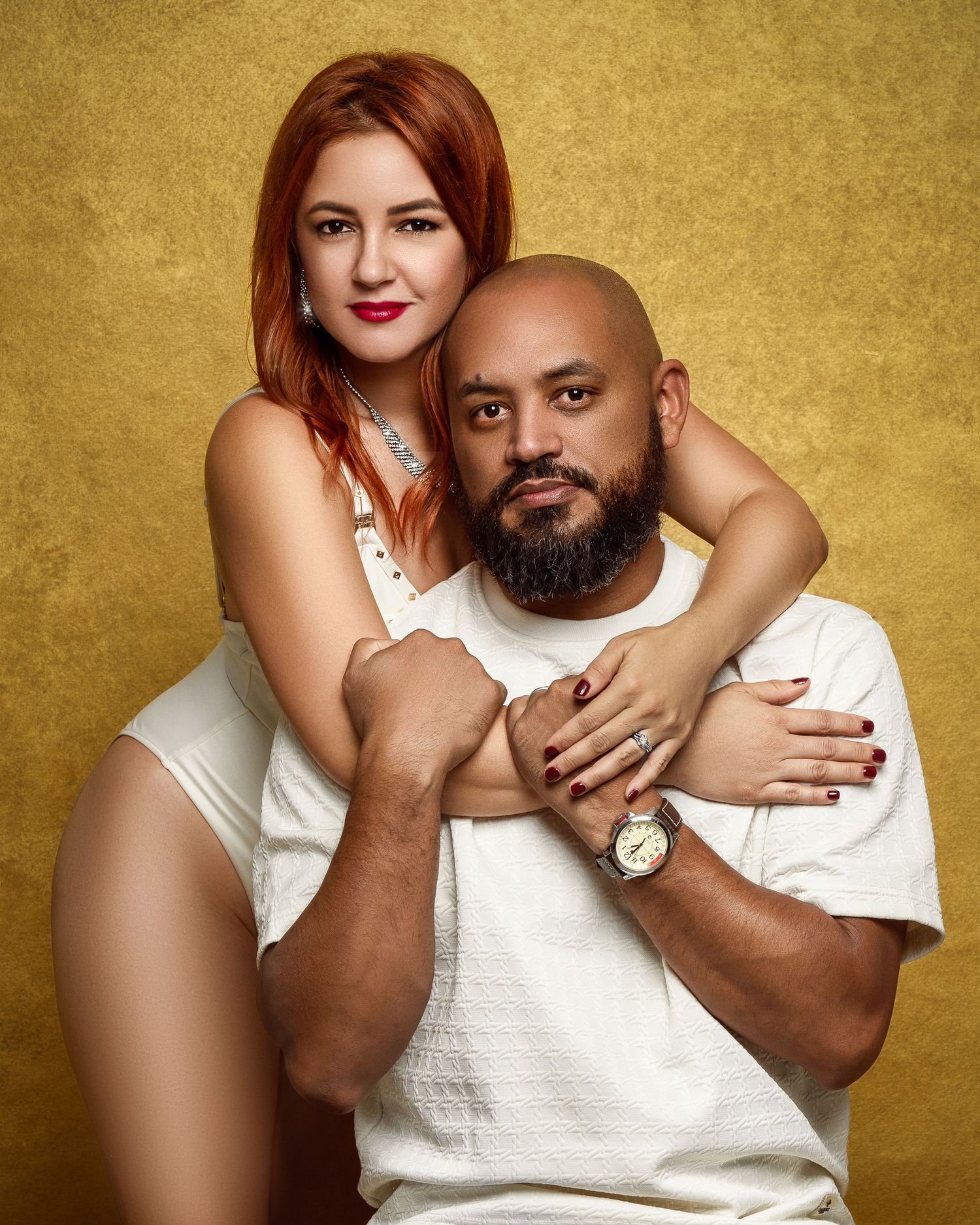 Couple in white outfits posing together against a gold backdrop for an intimate portrait session.