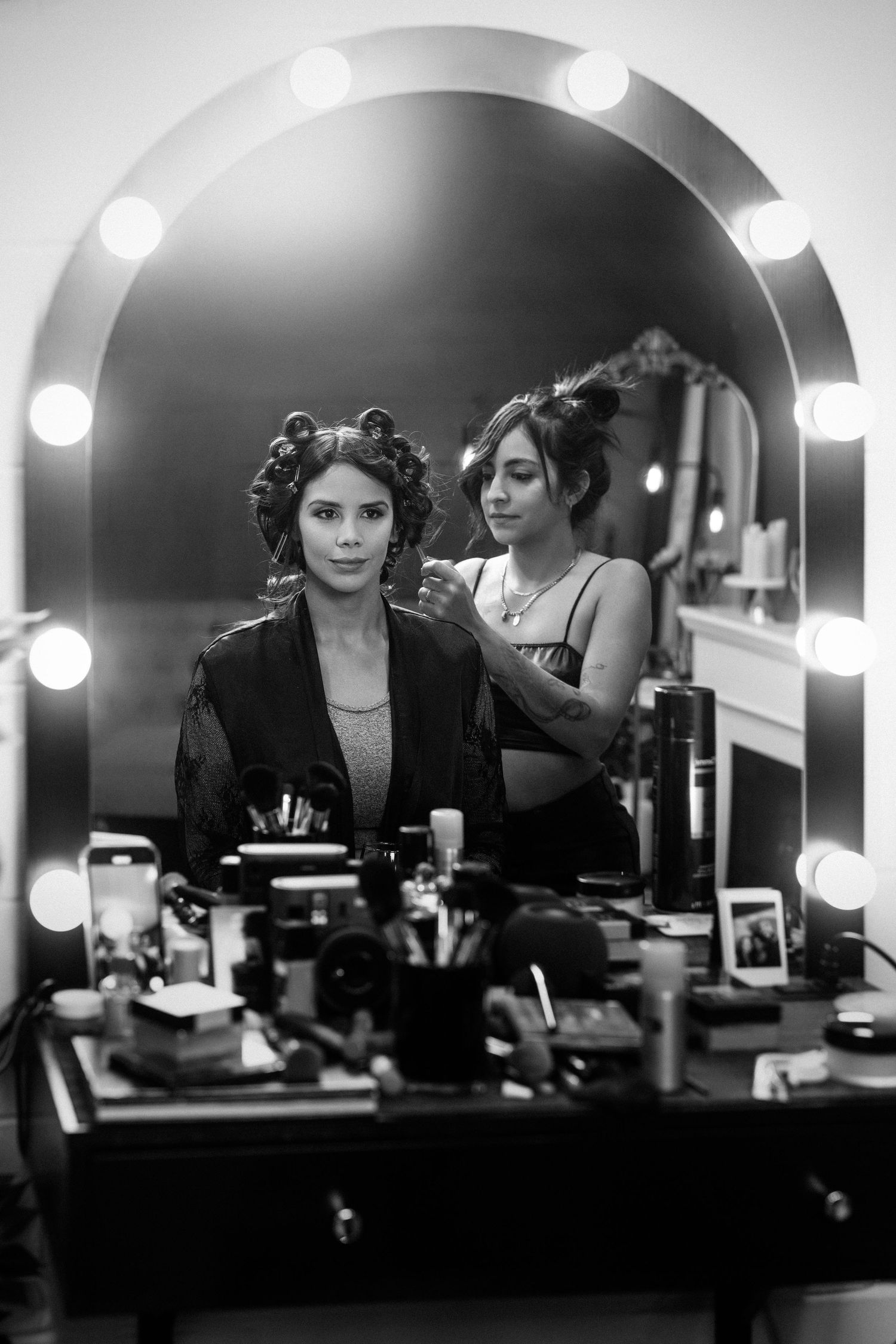 Black and white photo of backstage makeup preparation with vanity mirror lights.