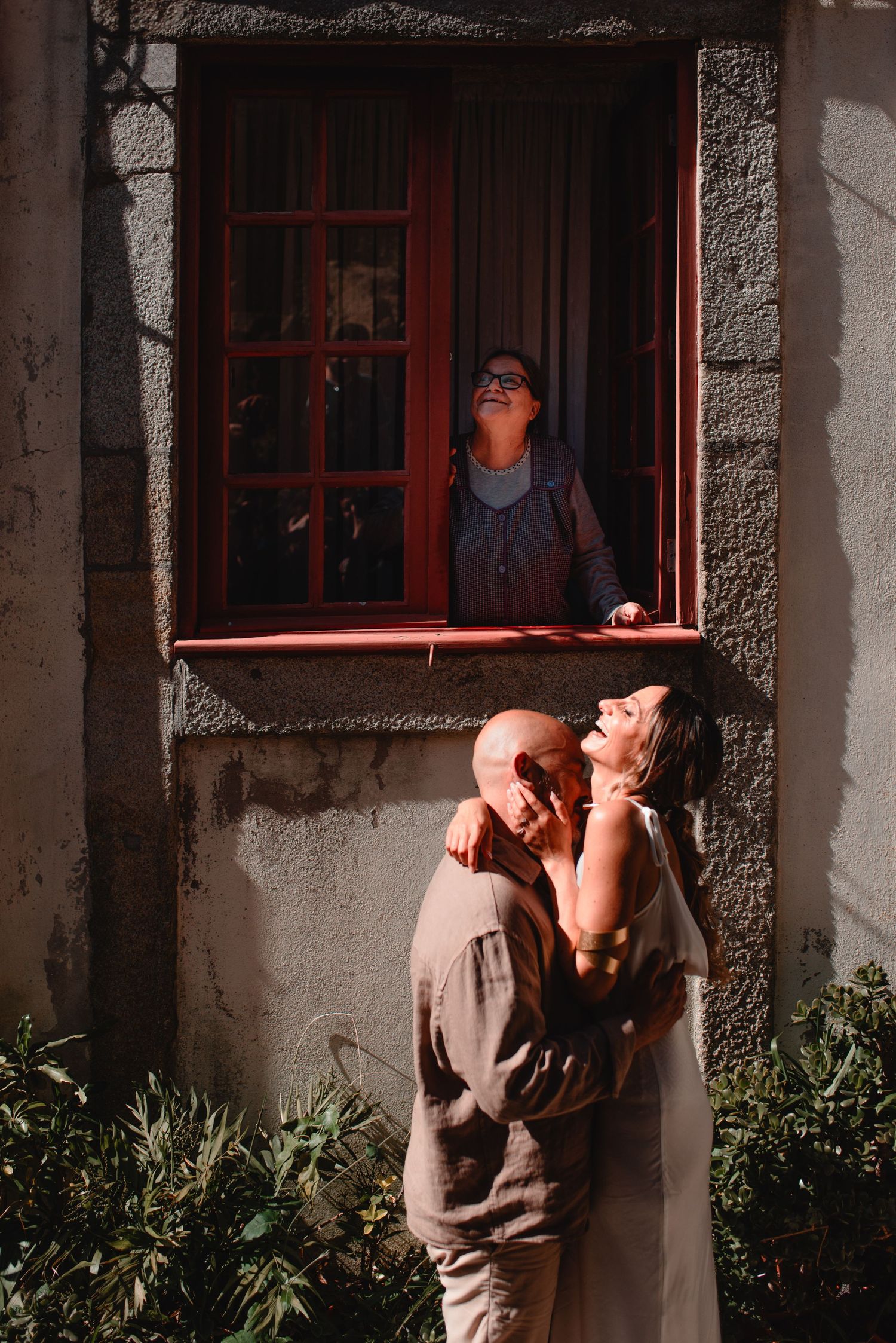 A romantic scene unfolds against weathered stone walls and red window frames.
