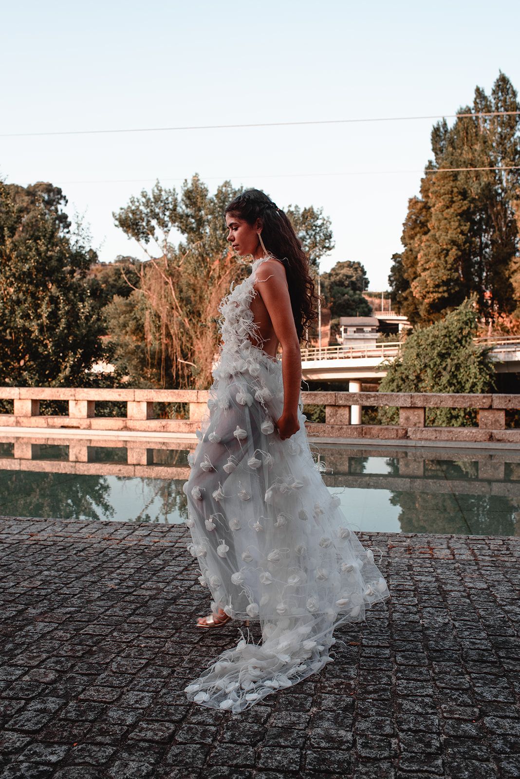 Ethereal white wedding dress flowing dramatically against a stone-paved surface at sunset.