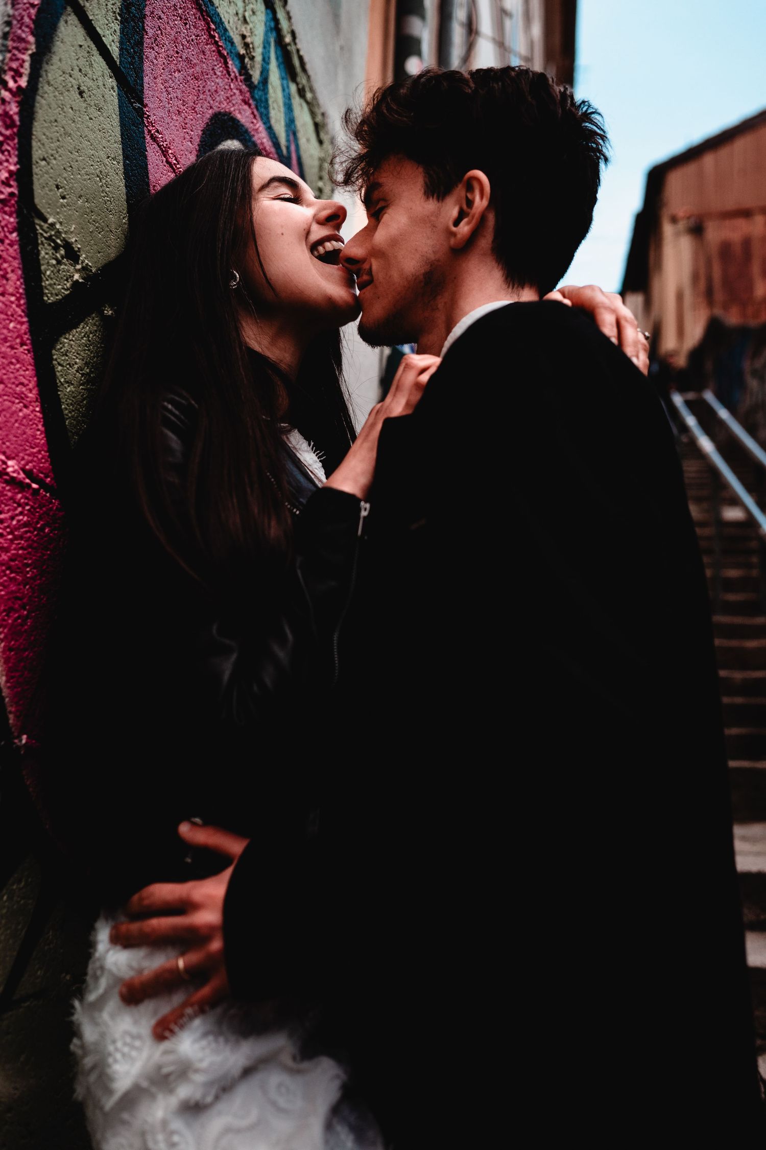 Couple sharing a romantic moment against a colorful graffiti wall in an urban setting.
