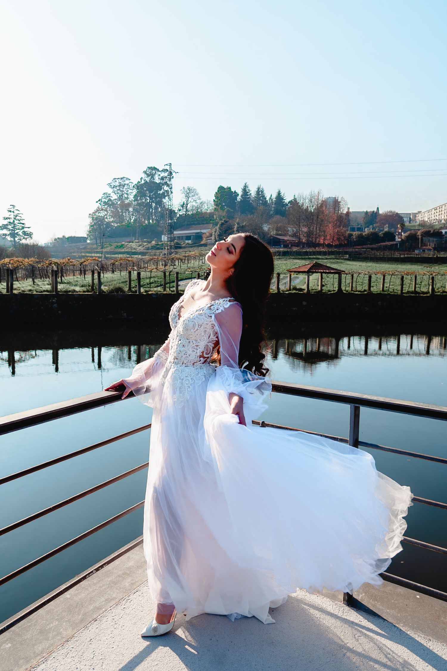 Person in white wedding dress twirling on dock by serene lake during daytime.