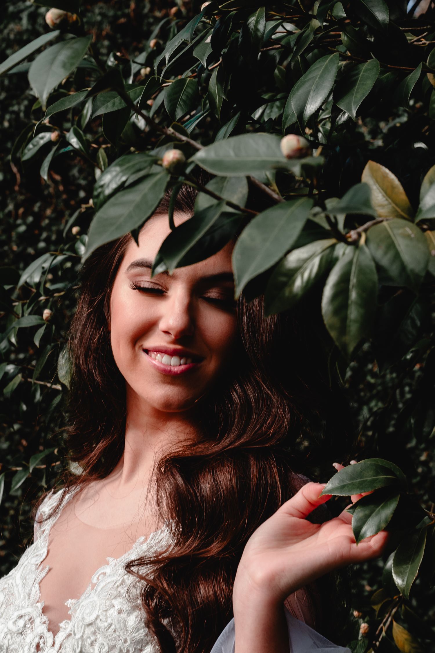Bride in lace dress smiles joyfully among green leaves and fruit in a garden setting.