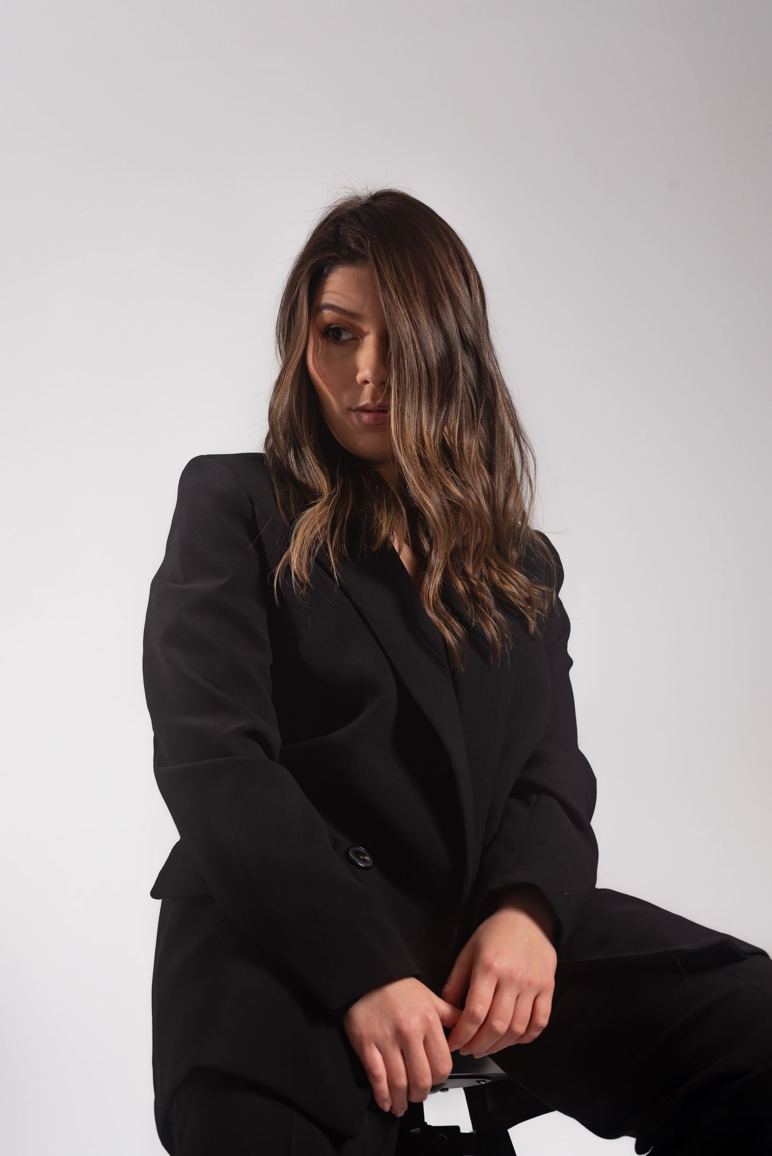 Moody studio portrait in black blazer against light gray background.