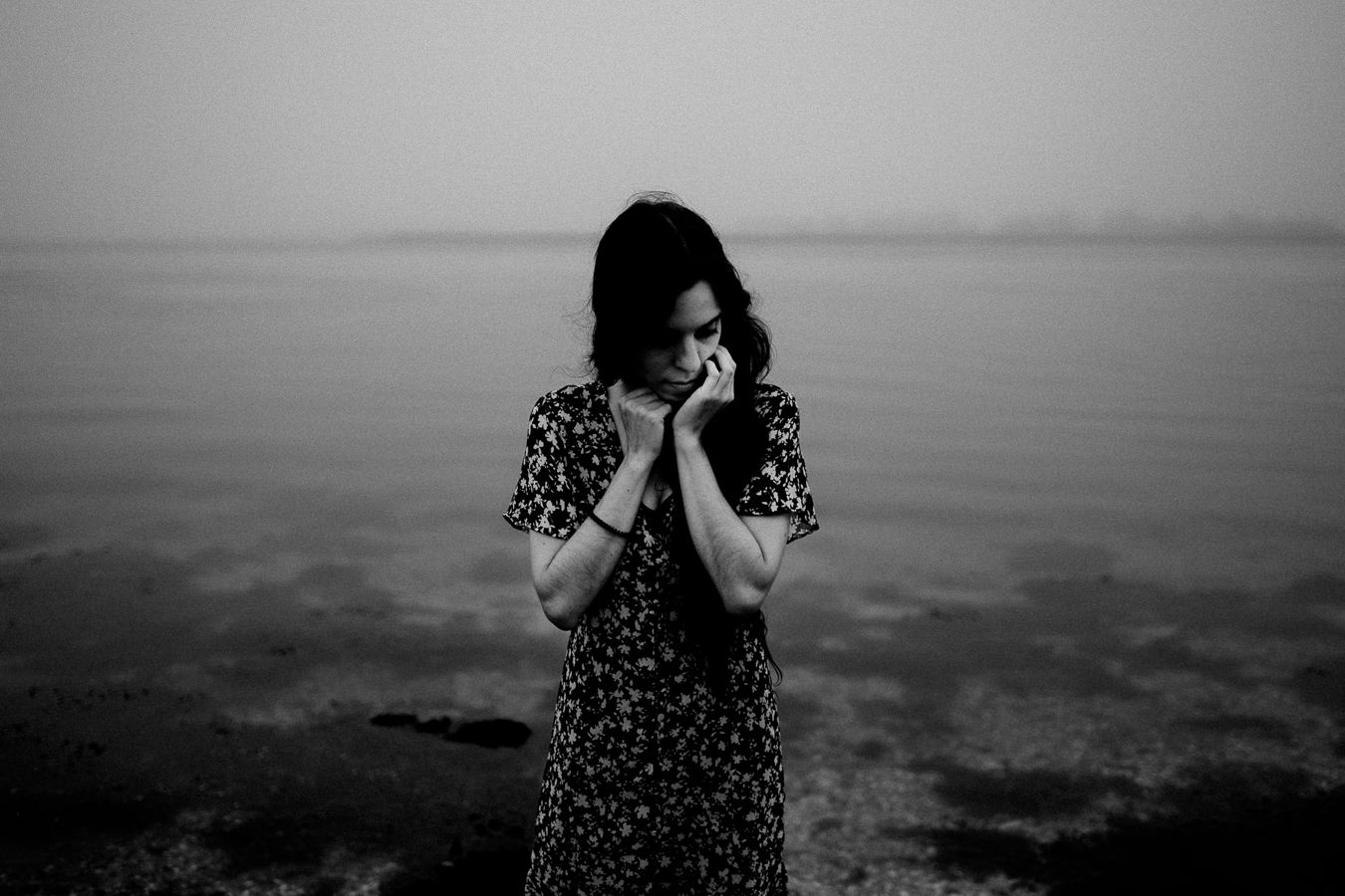Moody black and white portrait of a person in a floral dress against a misty backdrop.