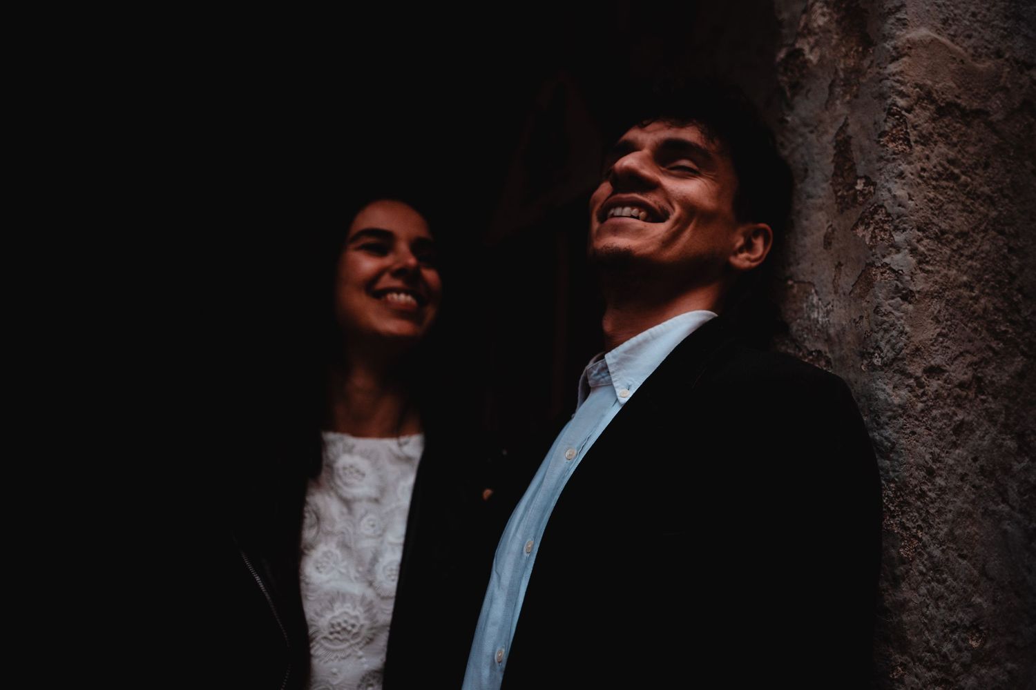 A smiling couple in elegant attire share a joyful moment together in a dimly lit setting.