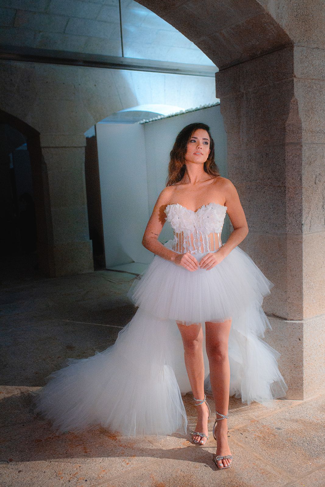 A modern bridal gown with layered tulle skirt photographed in an industrial concrete setting.