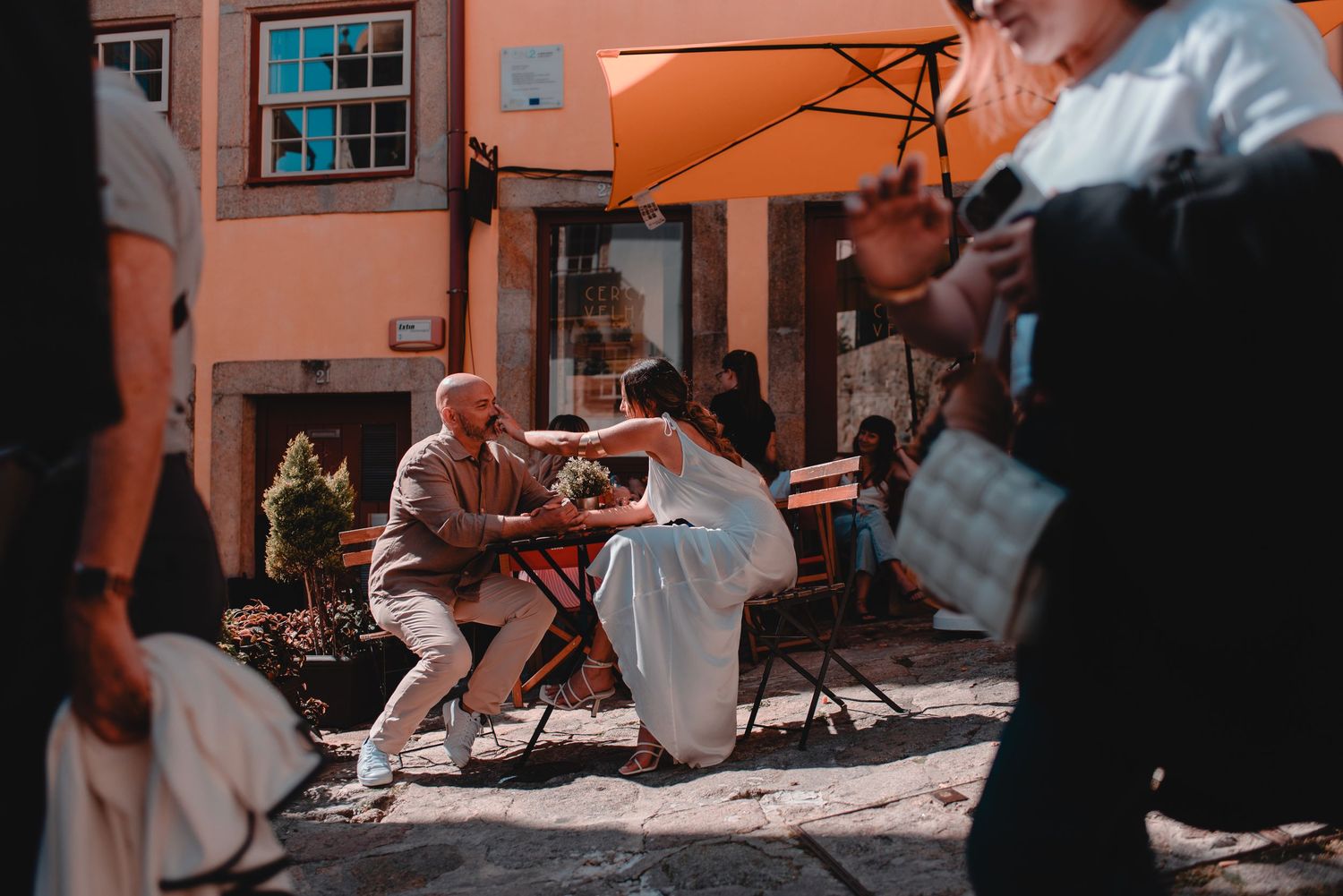 Warm sunlight illuminates a couple's embrace against an orange Mediterranean building facade.