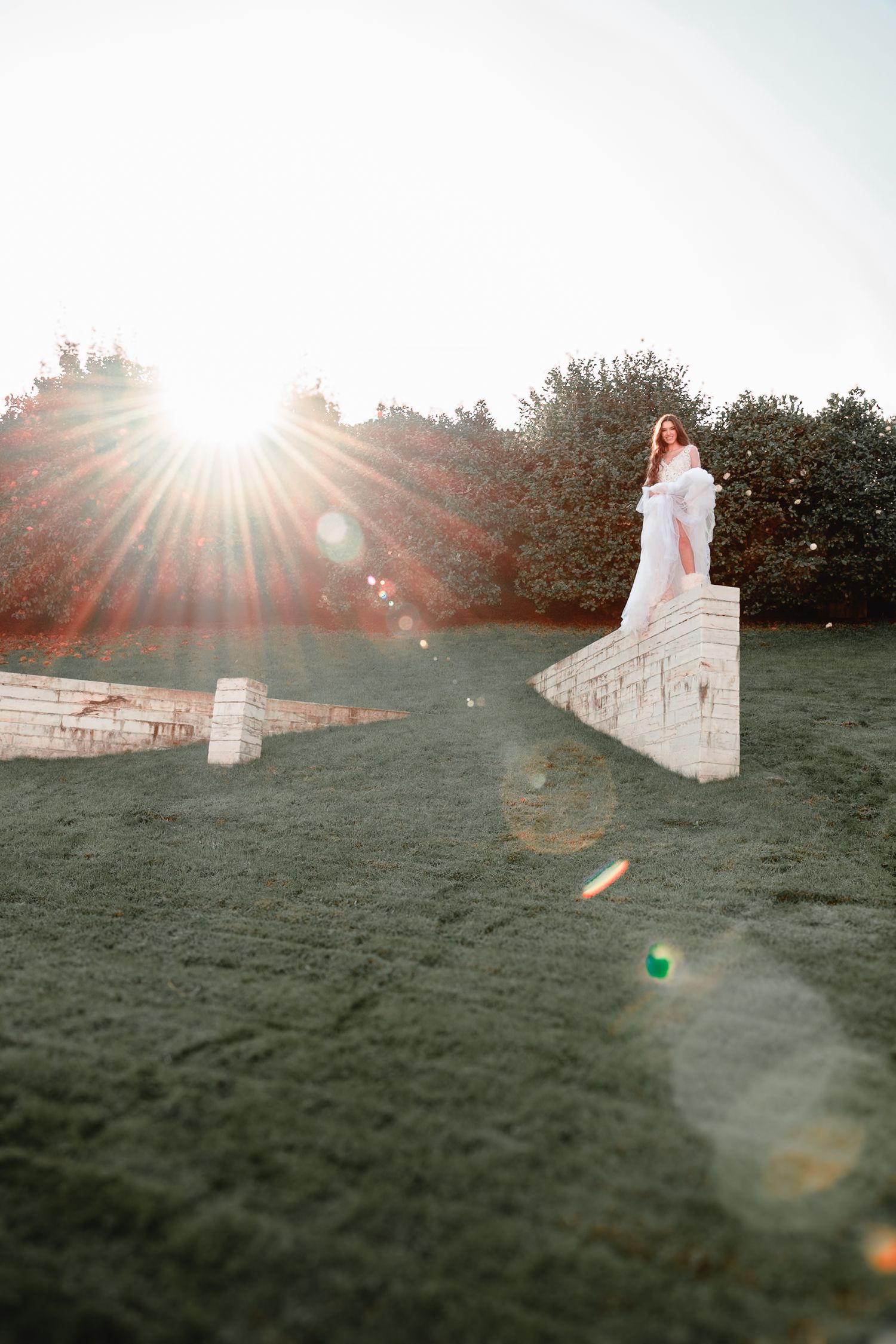 White dress flowing in the sunlight against stone walls on a grassy hillside during golden hour.
