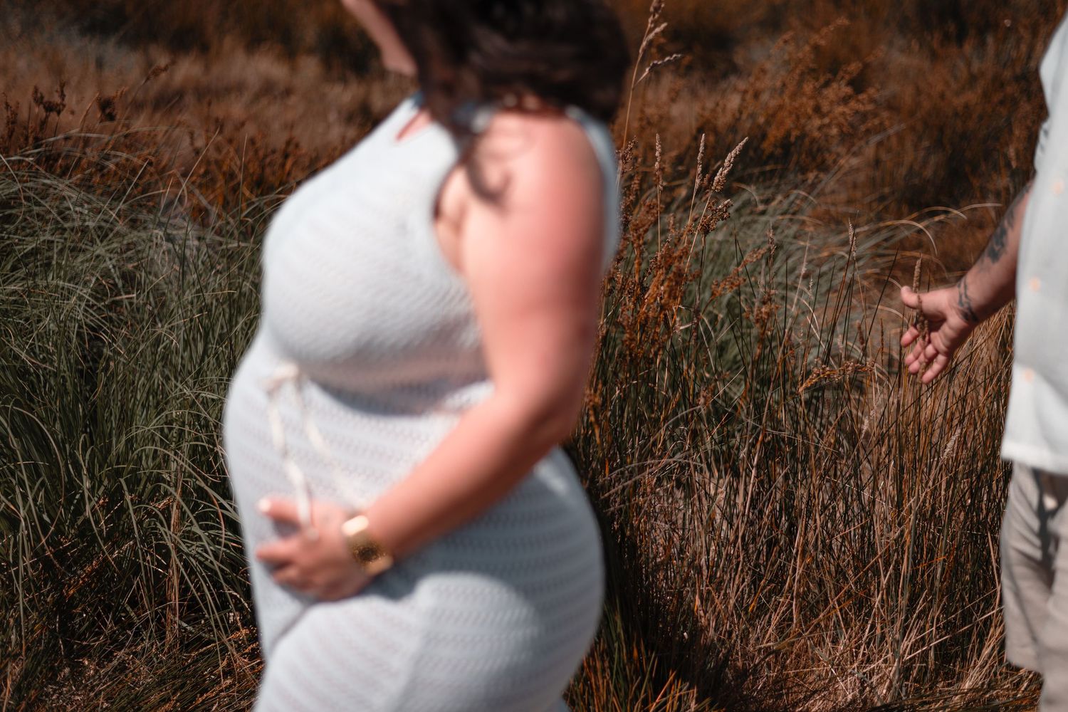 Maternity photos captured against white barn in natural desert landscape.