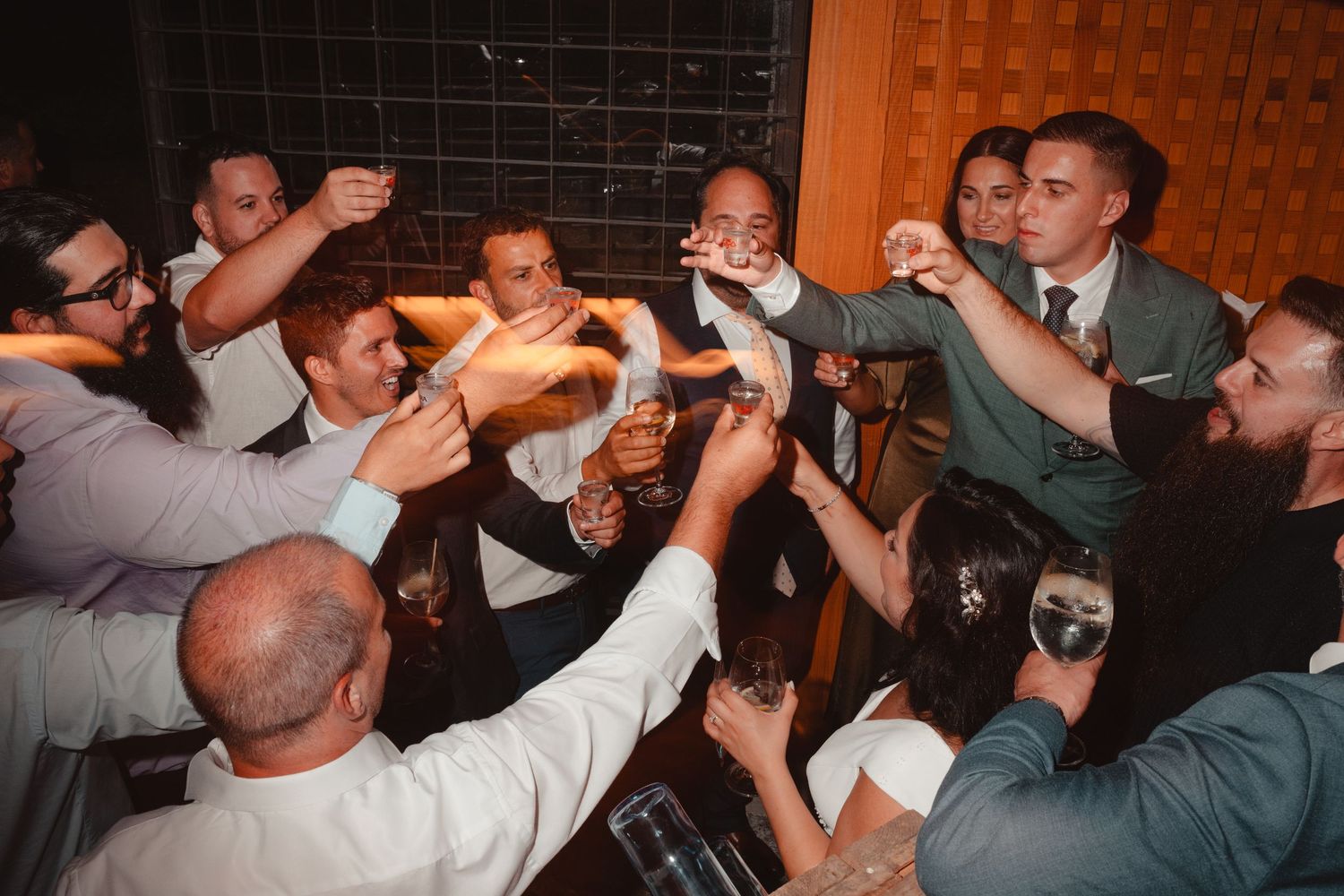 Group of men toasting drinks together at a lively wedding reception party celebration.
