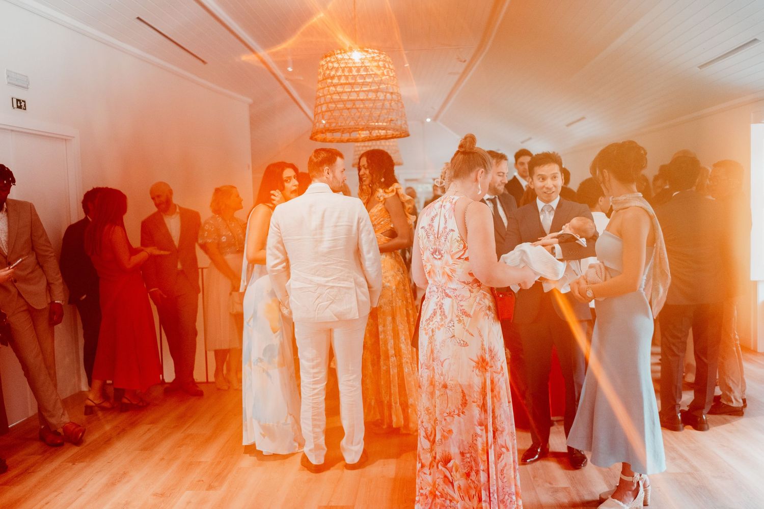 Guests dancing at an elegant wedding reception with warm orange lighting and a decorative chandelier overhead.