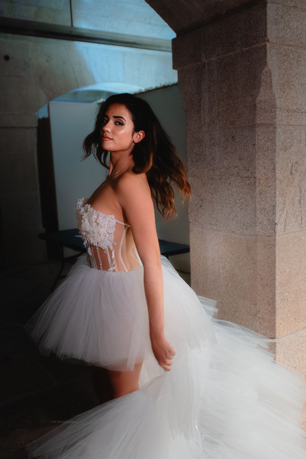An elegant tulle wedding gown with sheer bodice details photographed in an indoor architectural setting.