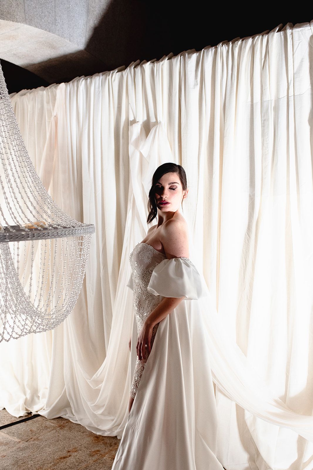 A romantic off-shoulder wedding dress photographed against flowing white curtain backdrops.