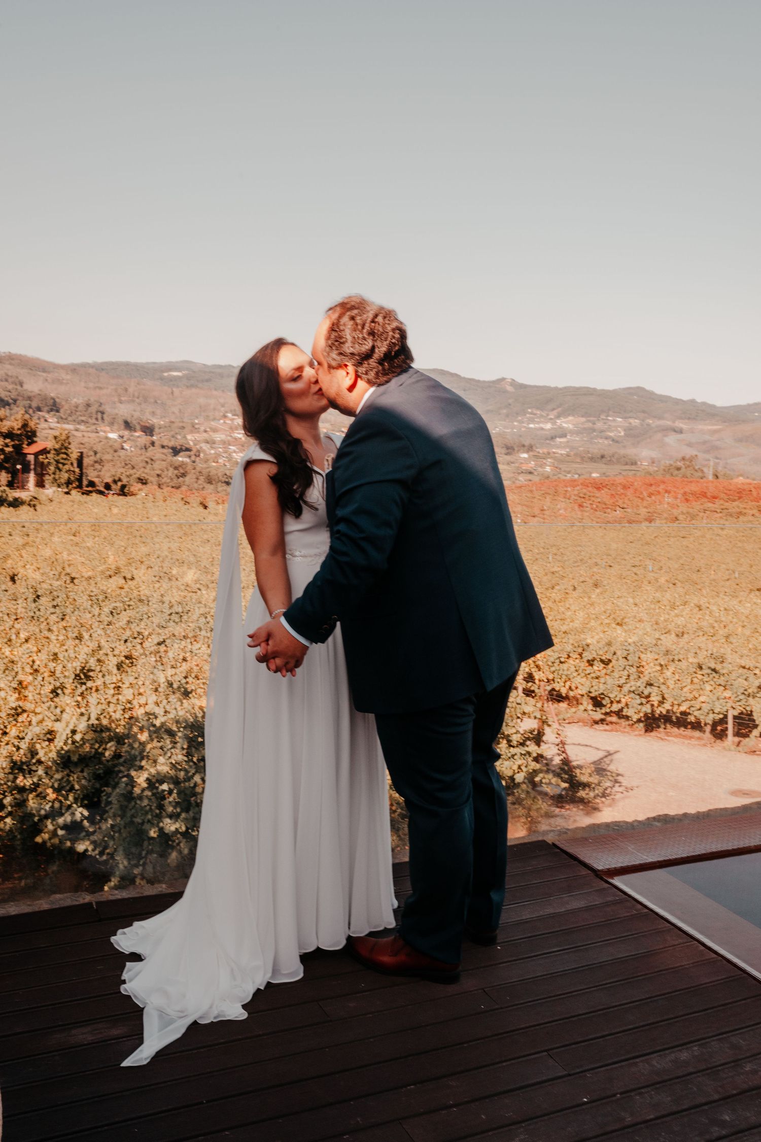 Bride and groom share a romantic kiss at a vineyard wedding venue with scenic mountain views in the background.