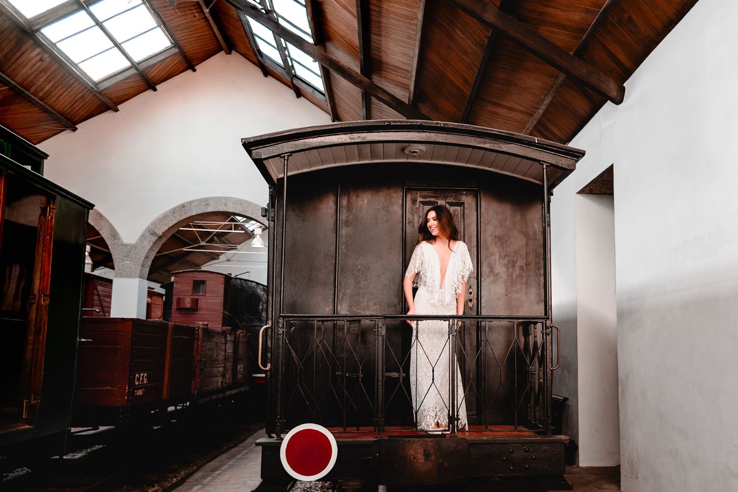 Artistic bridal portrait on vintage train car platform in flowing white dress.