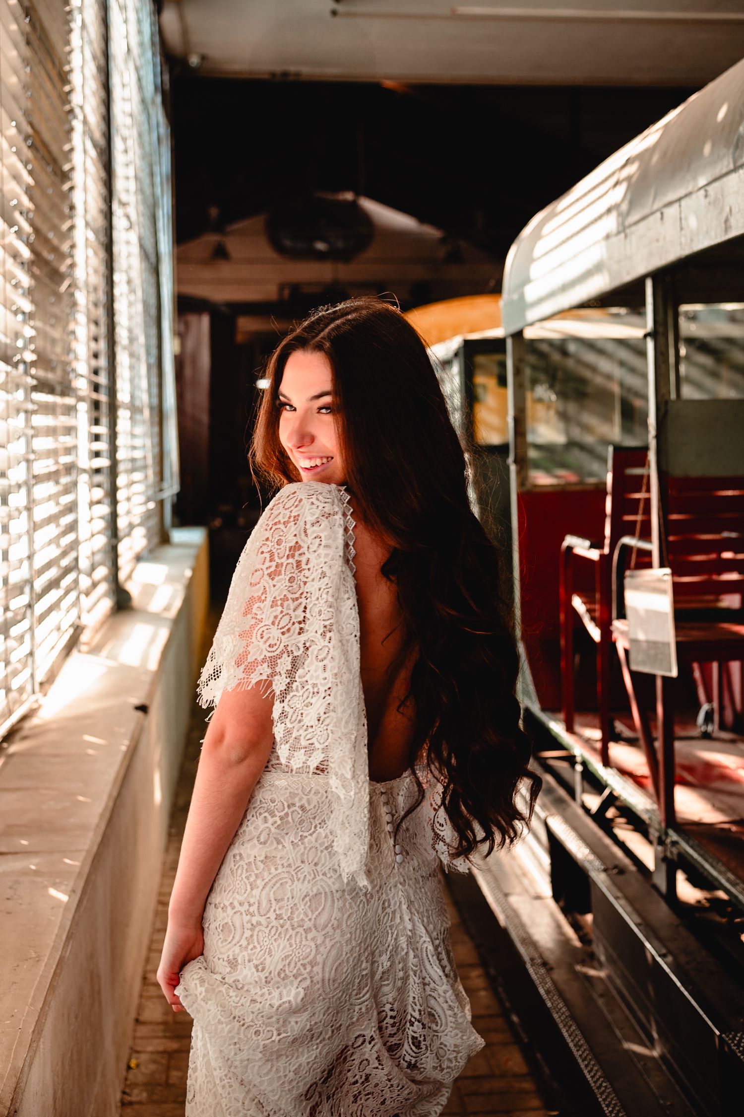 Sunlight streams through windows illuminating a white lace dress in vintage train setting.