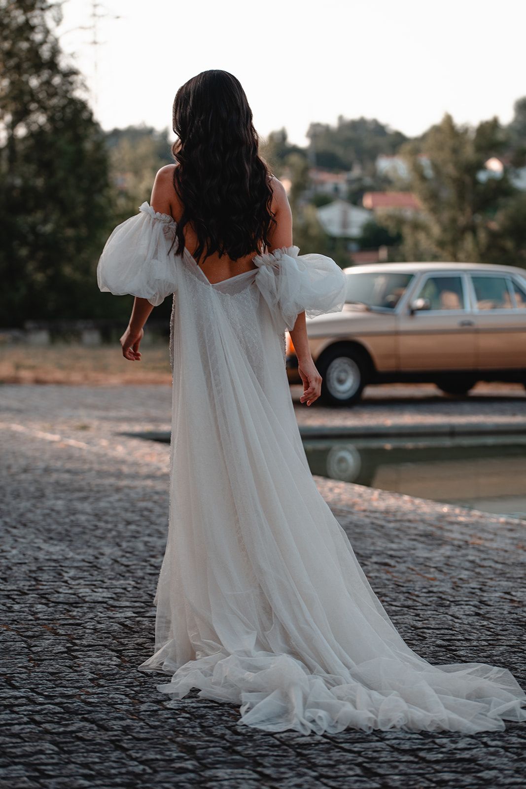 Wedding dress with long train trailing across stone pavement during golden hour.