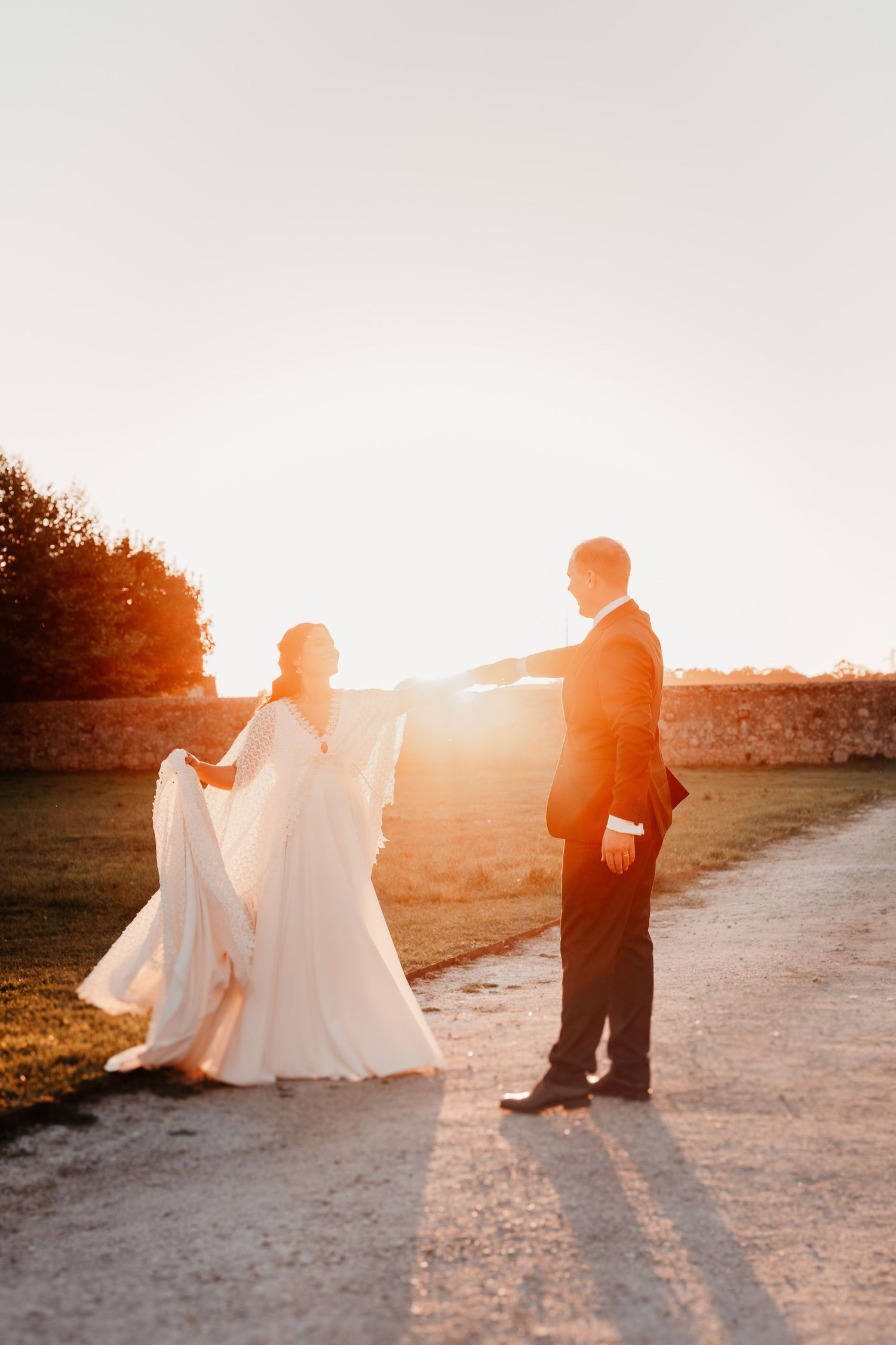 Bride and groom dancing at golden sunset on a gravel path, bride in flowing white gown, groom in black suit.