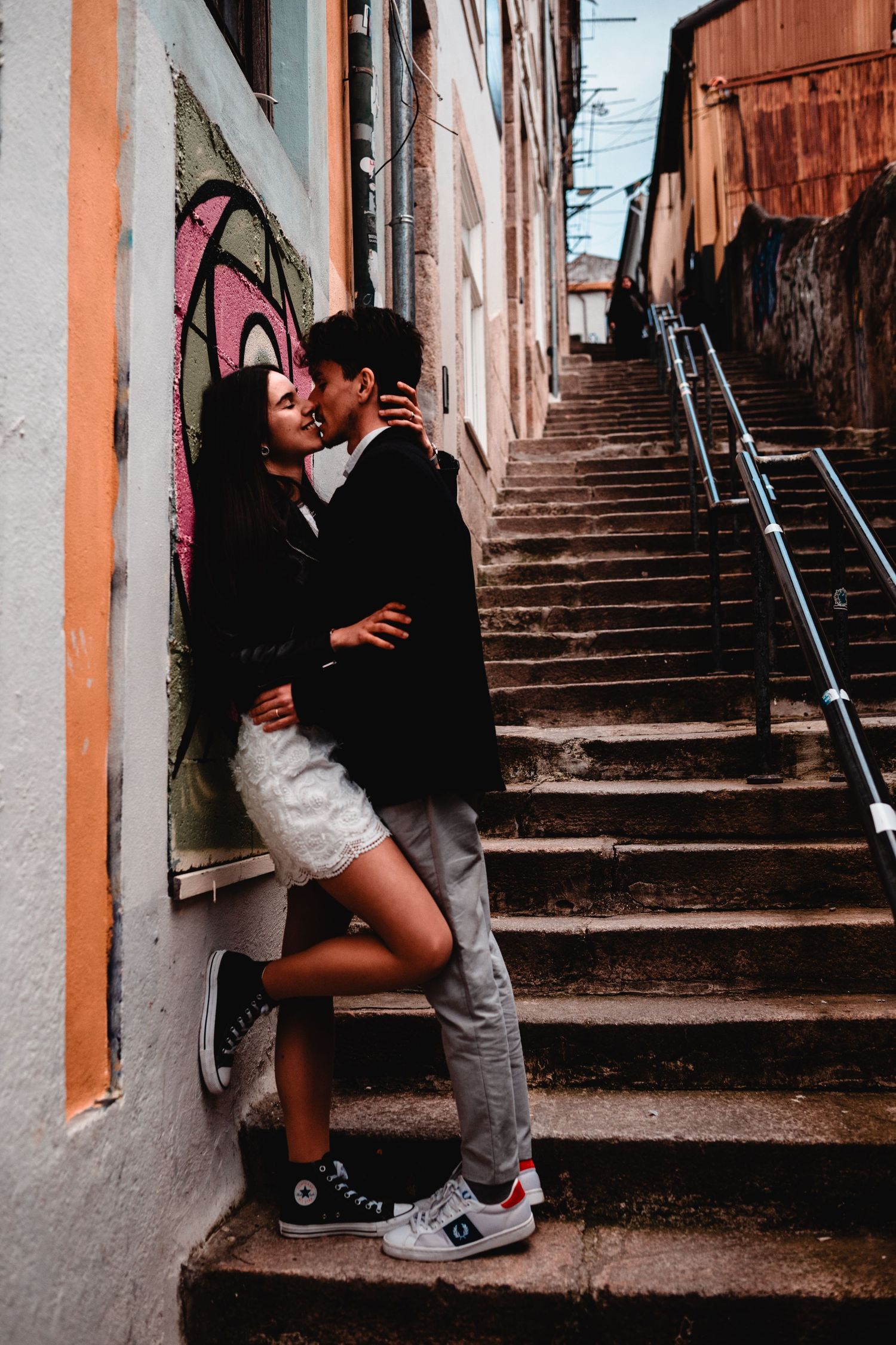 Young couple sharing a romantic moment on urban stairs with colorful graffiti wall backdrop.