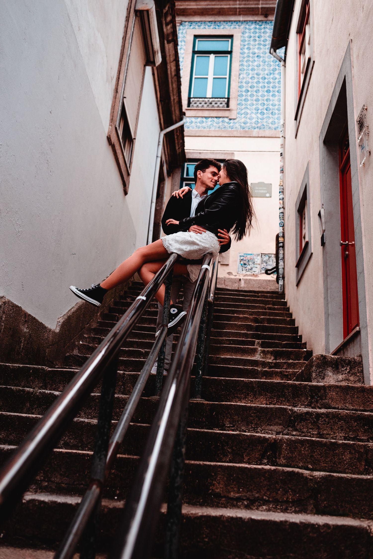 Romantic couple embracing on urban staircase between buildings with blue tiled facade in European city.