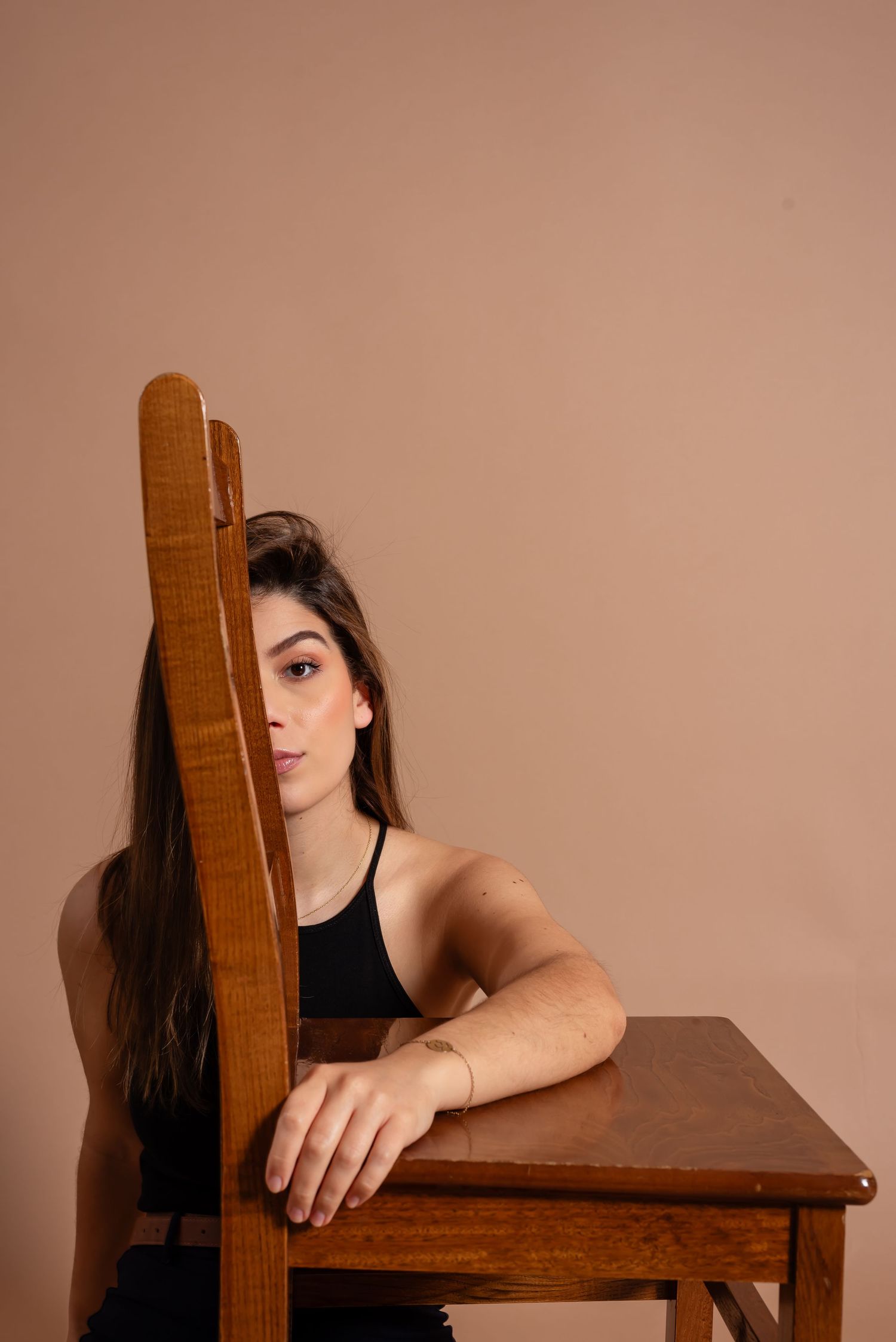 Creative portrait with model peeking from behind wooden chair back in studio setting.