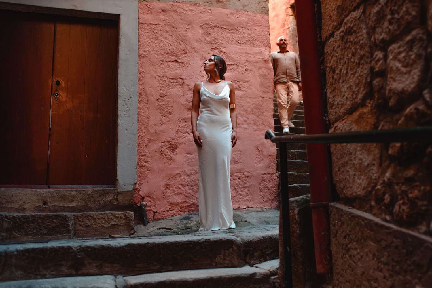 Couple in formal wear embraces in historic stone corridor with warm lighting.
