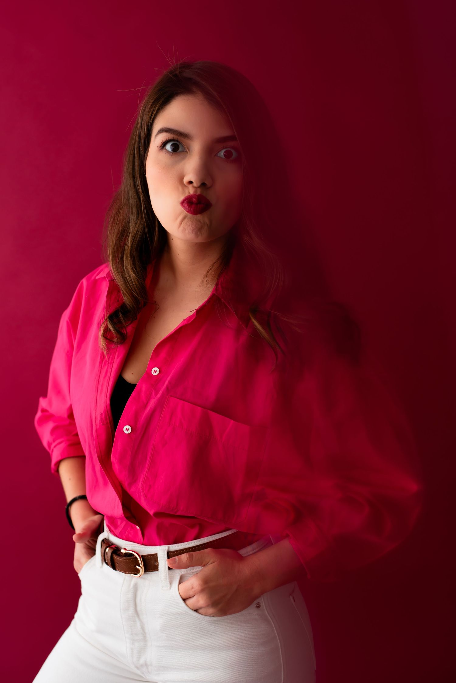 Fashion portrait against vibrant red background featuring bright pink button-down shirt.
