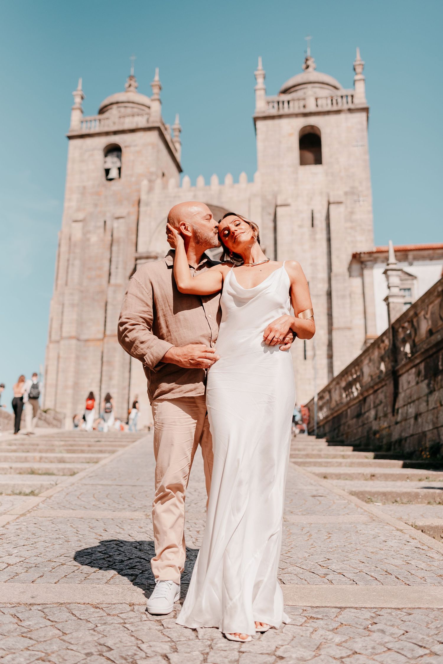 Couple sharing a kiss in wedding attire on cobblestone steps outside a historic cathedral in Porto, Portugal.