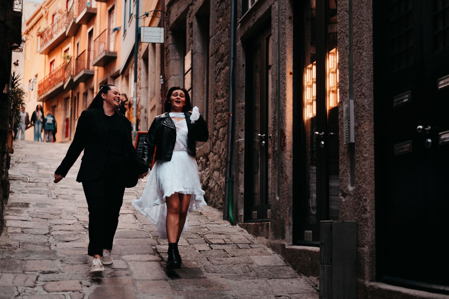Two women walking and laughing together on a charming cobblestone street in a European city.