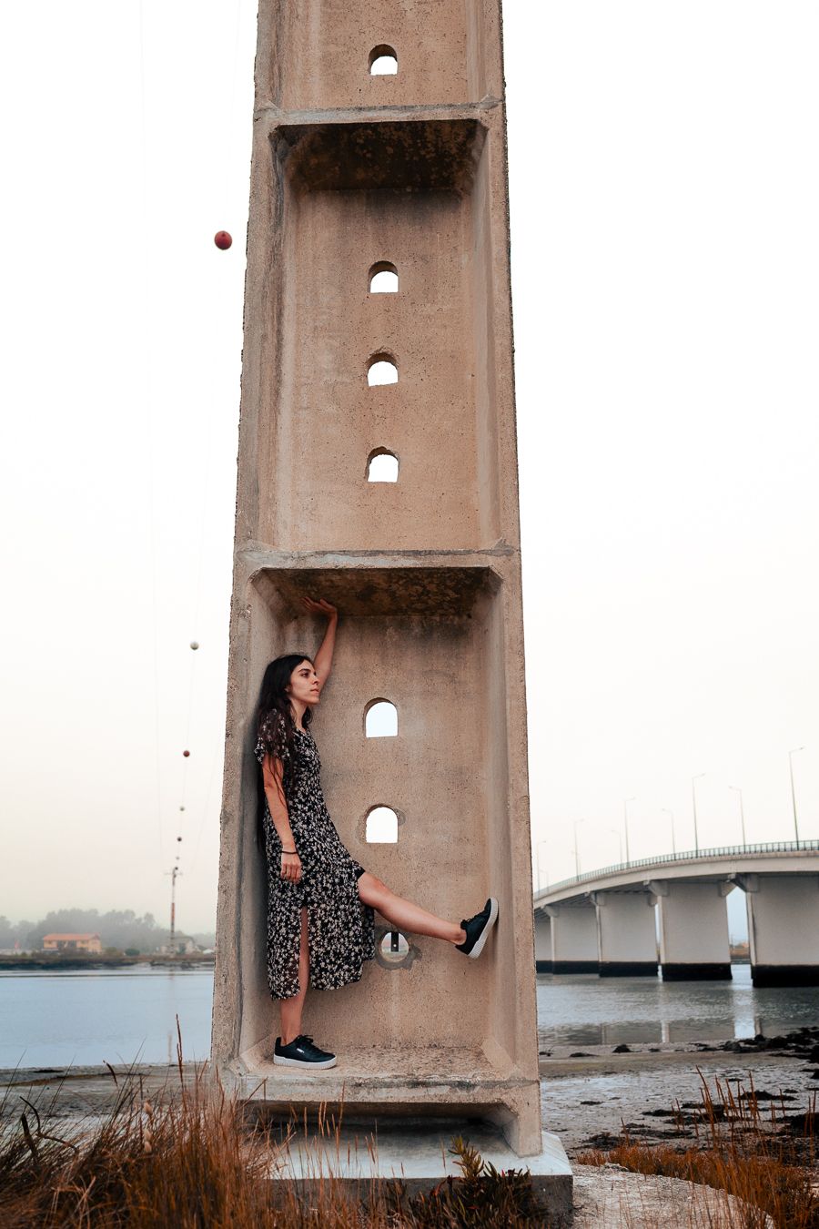 A figure in a polka dot dress poses creatively inside a concrete structure near a bridge.