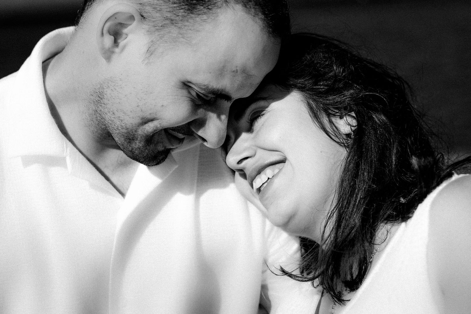 Black and white portrait of couple touching foreheads and smiling in soft light.