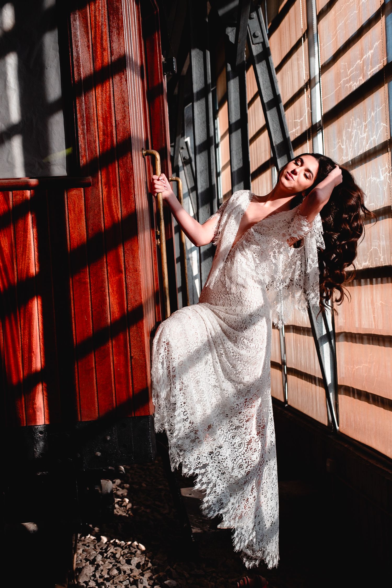 White lace dress photographed in moody lighting with dramatic shadows against red wooden wall.
