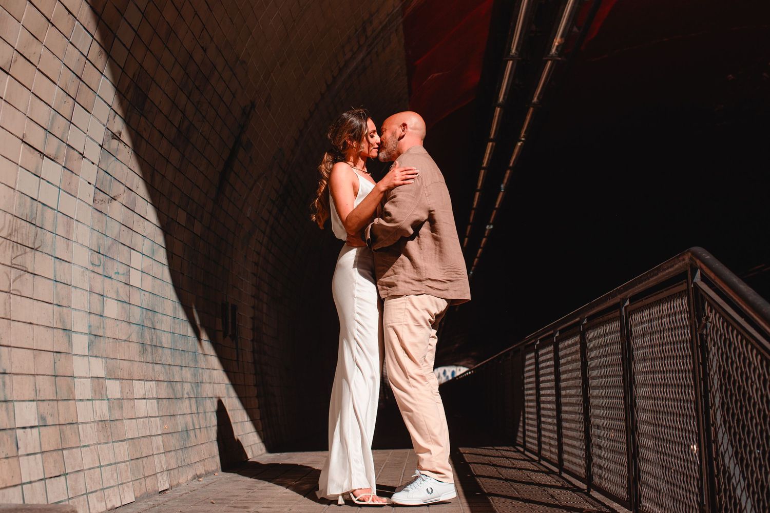 Couple in elegant attire shares tender moment in historic stone passageway.
