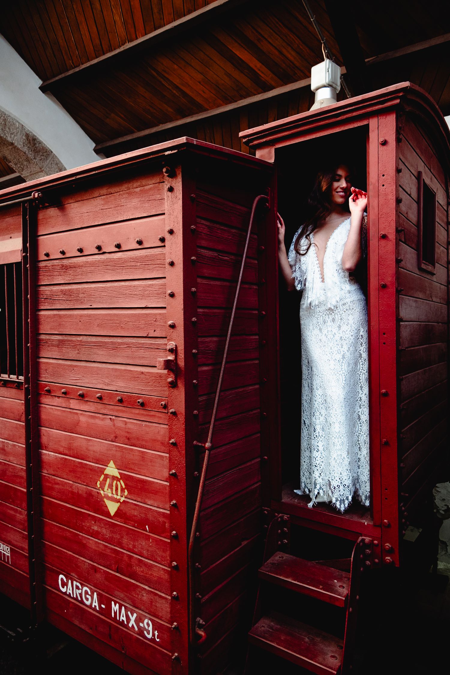 A flowing white wedding gown displayed against rustic red wooden railway car walls.