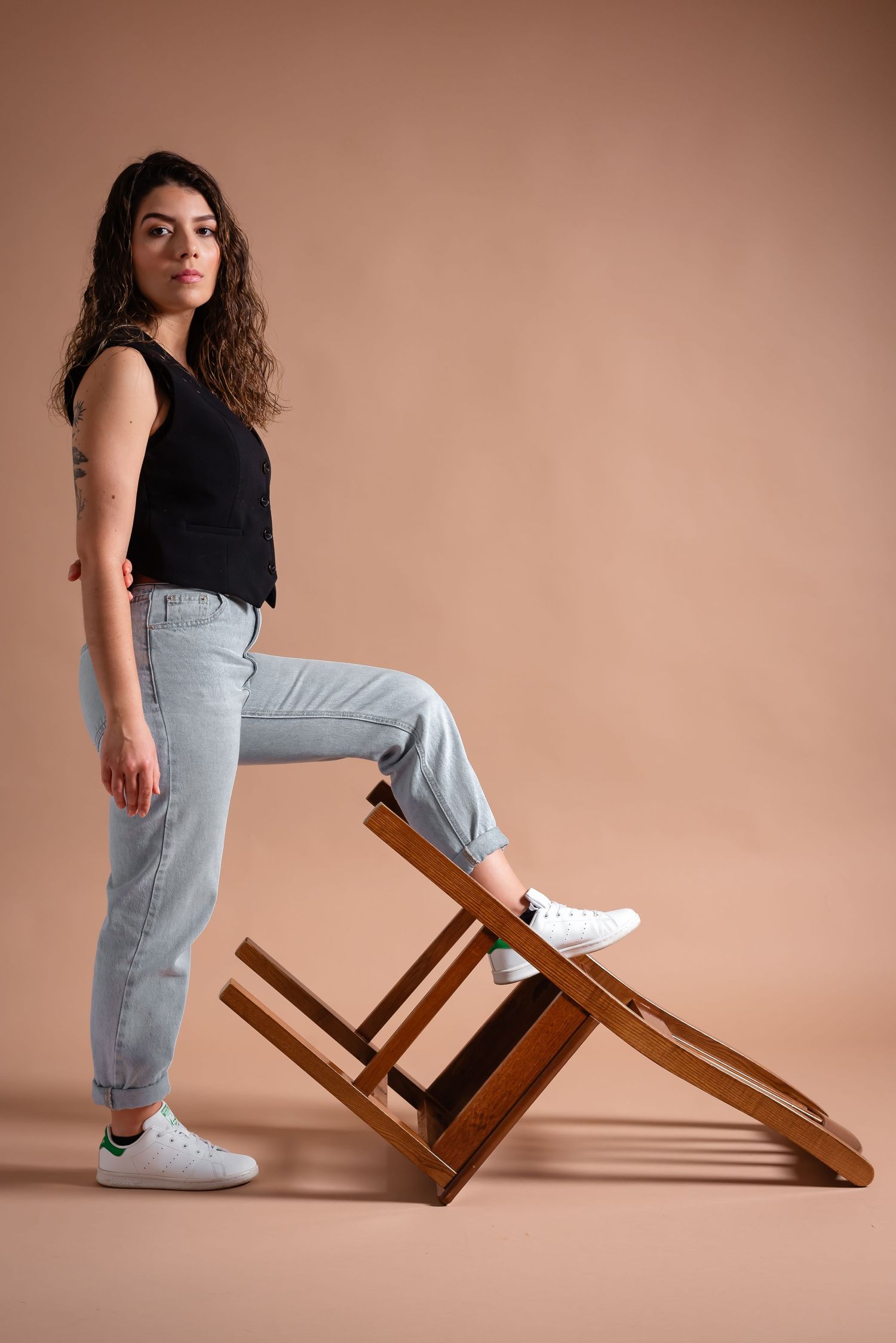 Casual studio portrait with angled wooden chair creating geometric composition.