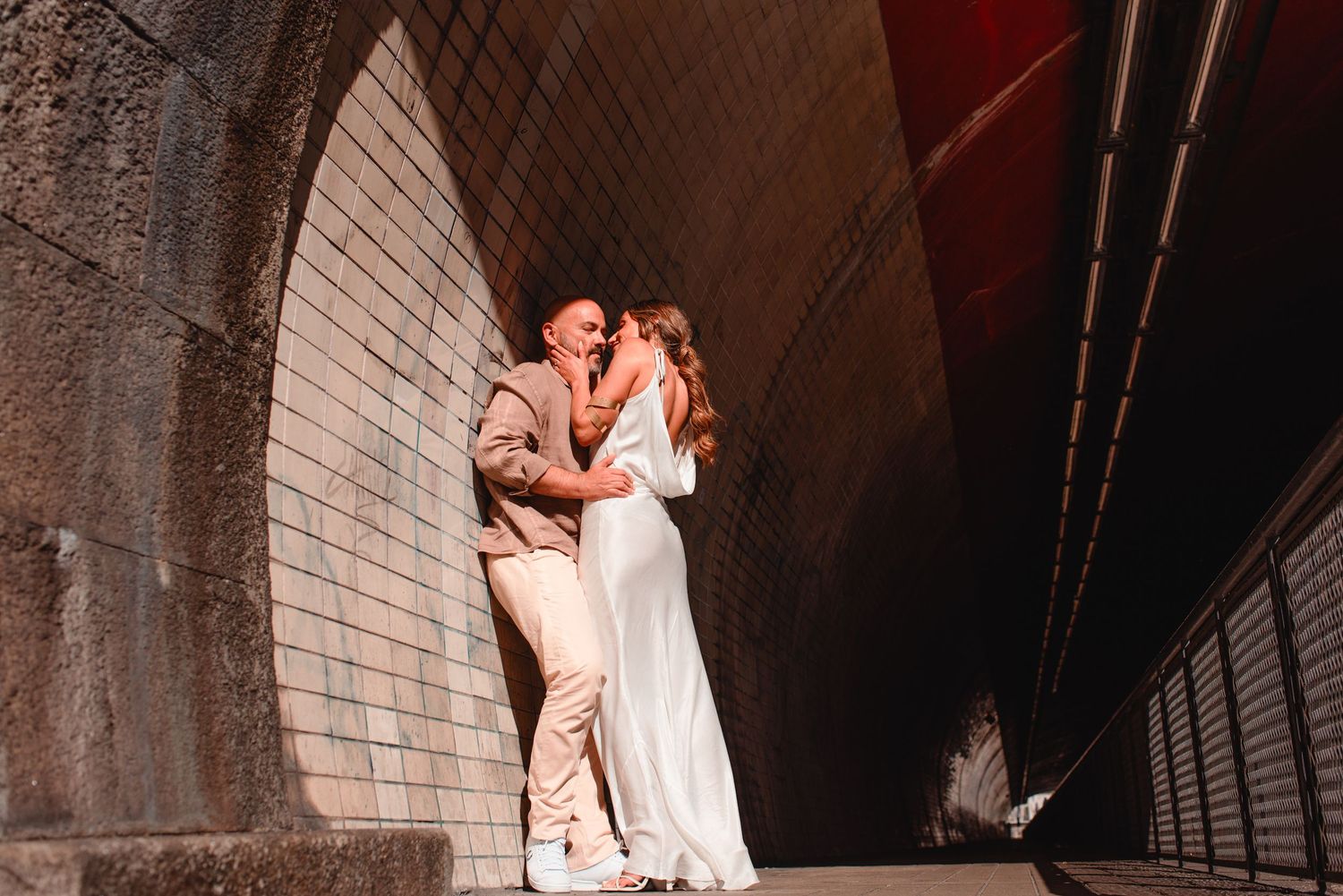 Romantic couple shares an intimate moment against a brick wall in dim lighting.
