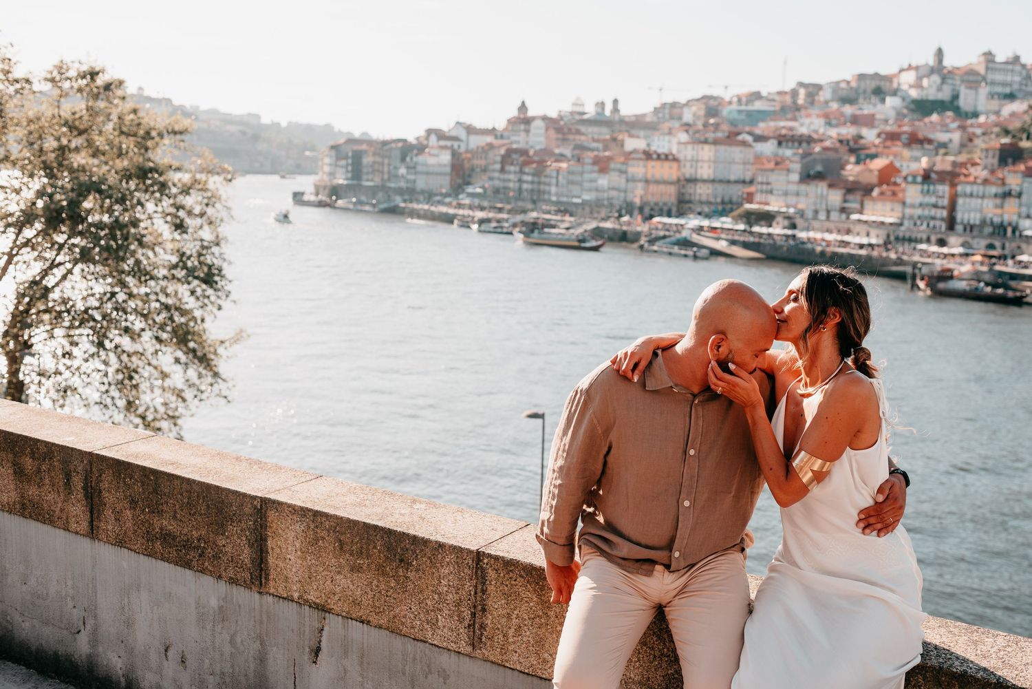 Couple sharing a romantic moment by the Douro River in Porto, with colorful cityscape in the background.