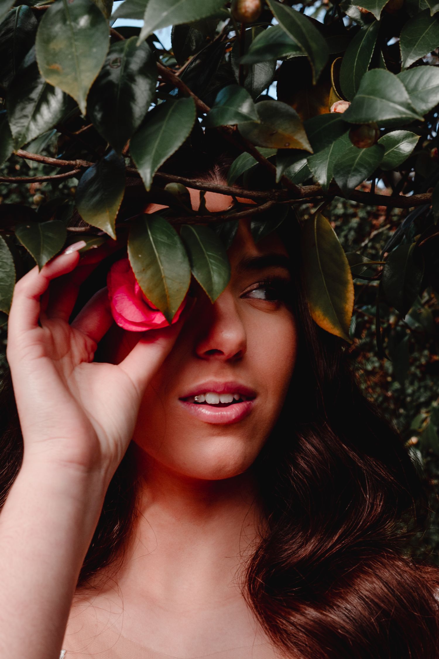 Artistic portrait through green foliage with red lip detail.