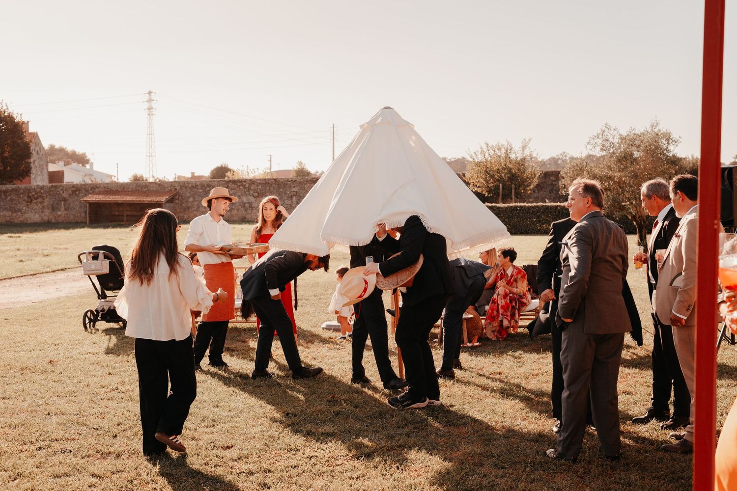 Guests playing limbo near a white teepee tent at an outdoor wedding reception on a sunny day.