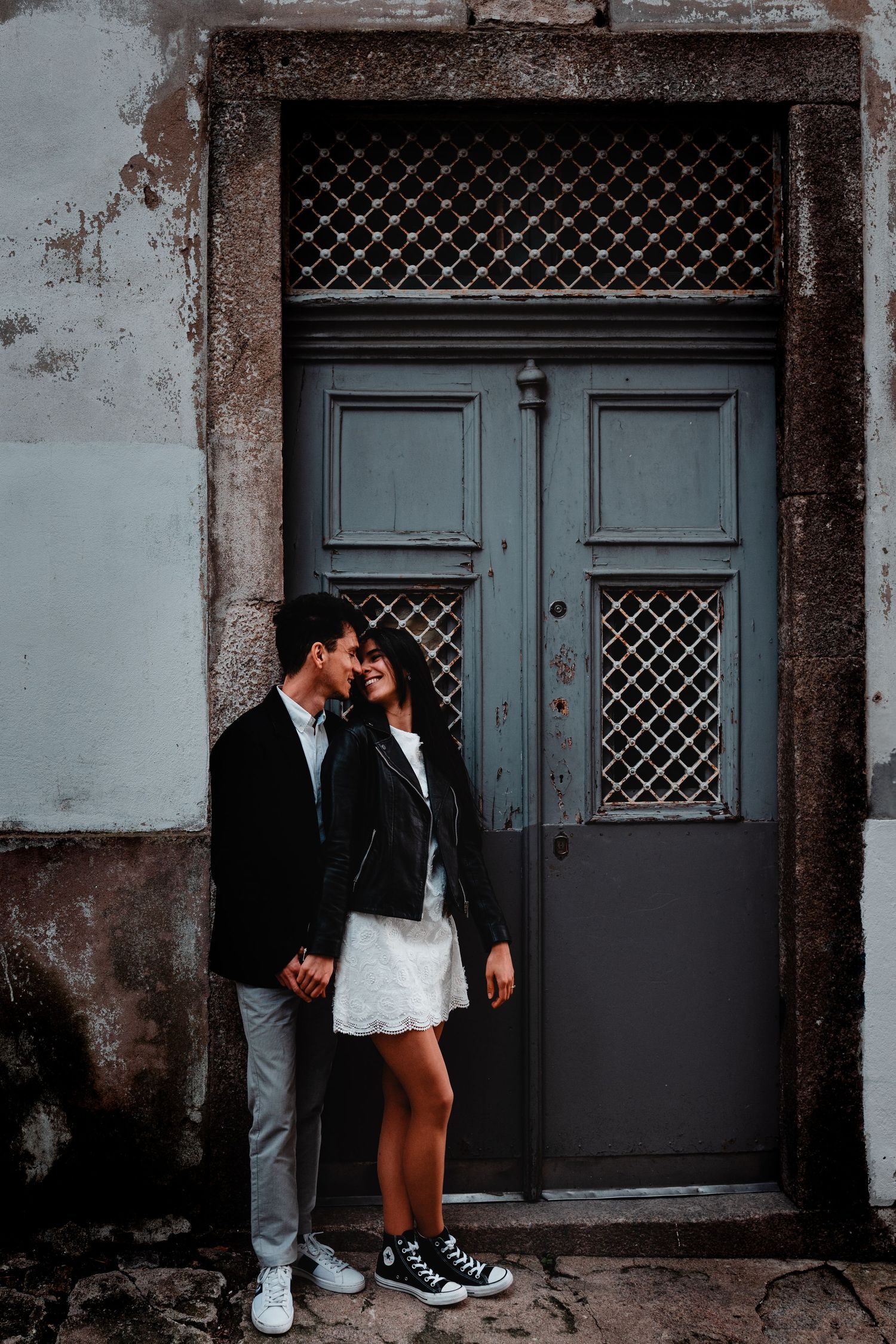 Romantic couple standing close together in front of a vintage gray door on a weathered stone building.