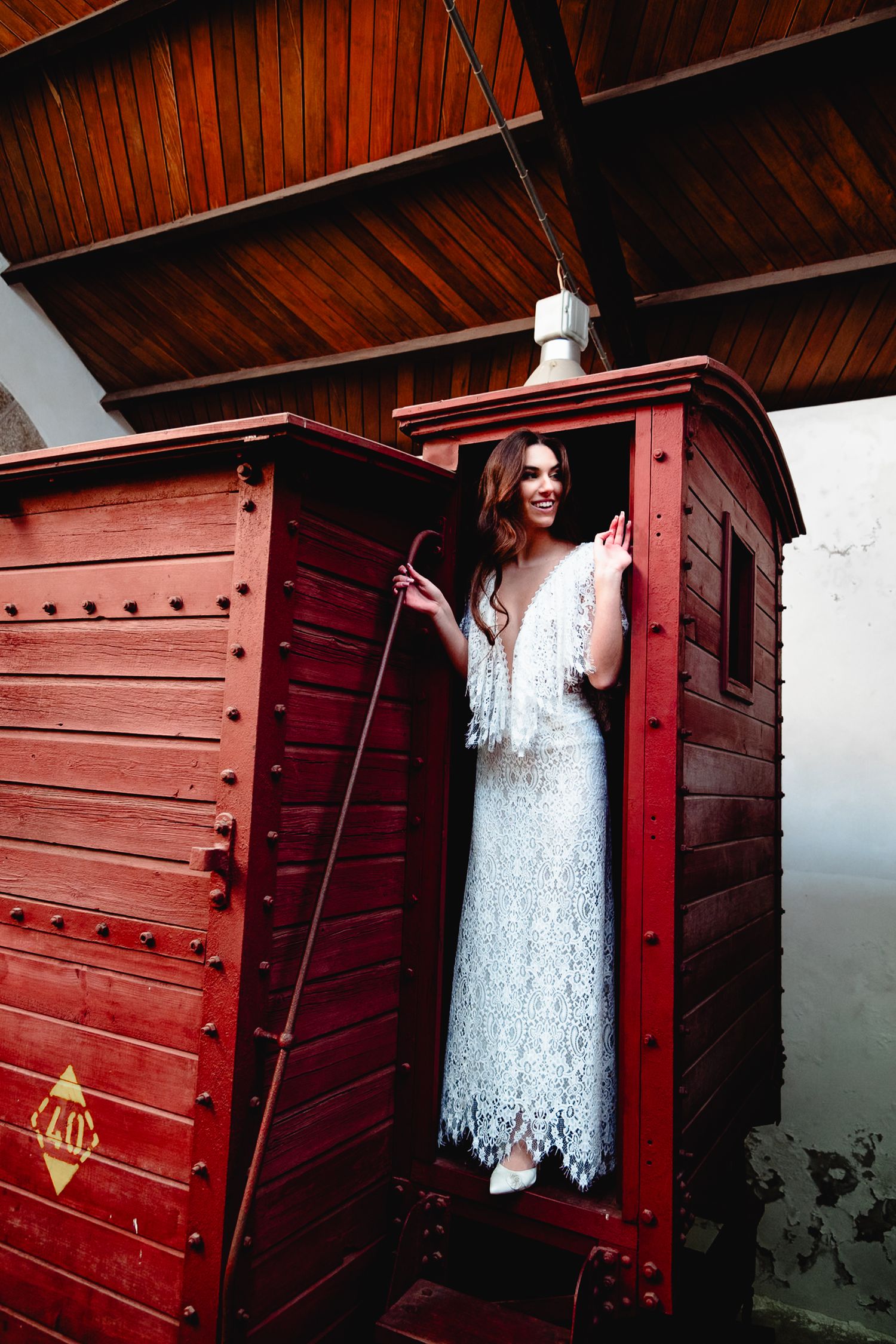 Joyful moment captured in vintage red train car doorway wearing flowing lace wedding dress.
